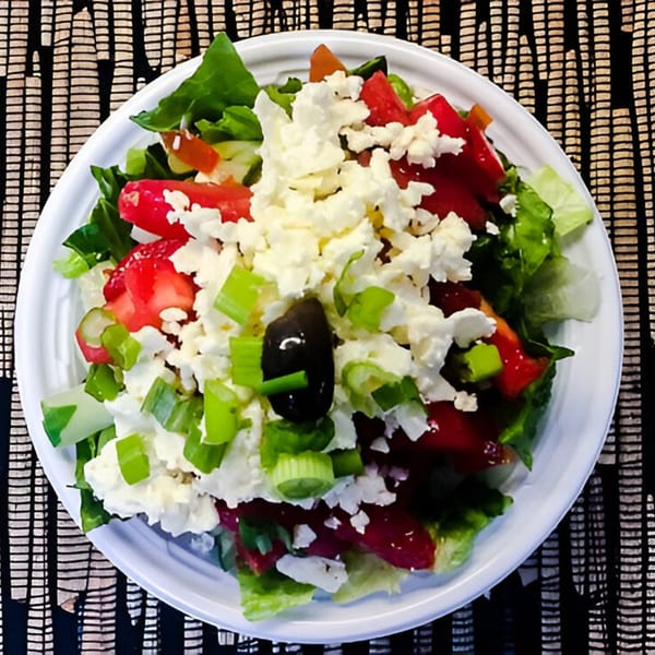 Woody's Famous Salads' fresh salad with lettuce, tomatoes, feta, green onions, and a black olive.