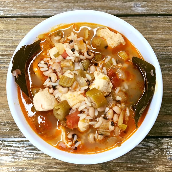 Hearty chicken and vegetable soup with rice, black-eyed peas, and bay leaves in a white bowl.