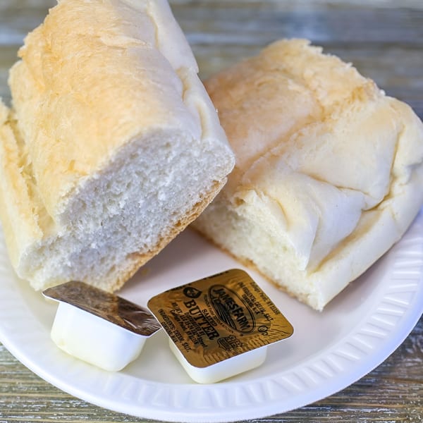 Two pieces of white bread and two James Farm butter packets on a white plate.