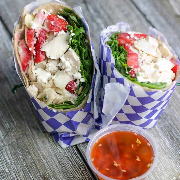 Two Woody's Famous Salads wraps with chicken, strawberries, and feta, with a side of dressing.