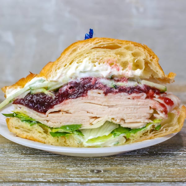 Half of a turkey and cranberry croissant sandwich with lettuce and creamy dressing on a white plate.